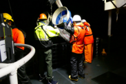 Crew members aboard a research vessel deploy bongo nets at night. All crew are wearing high visibility safety gear.