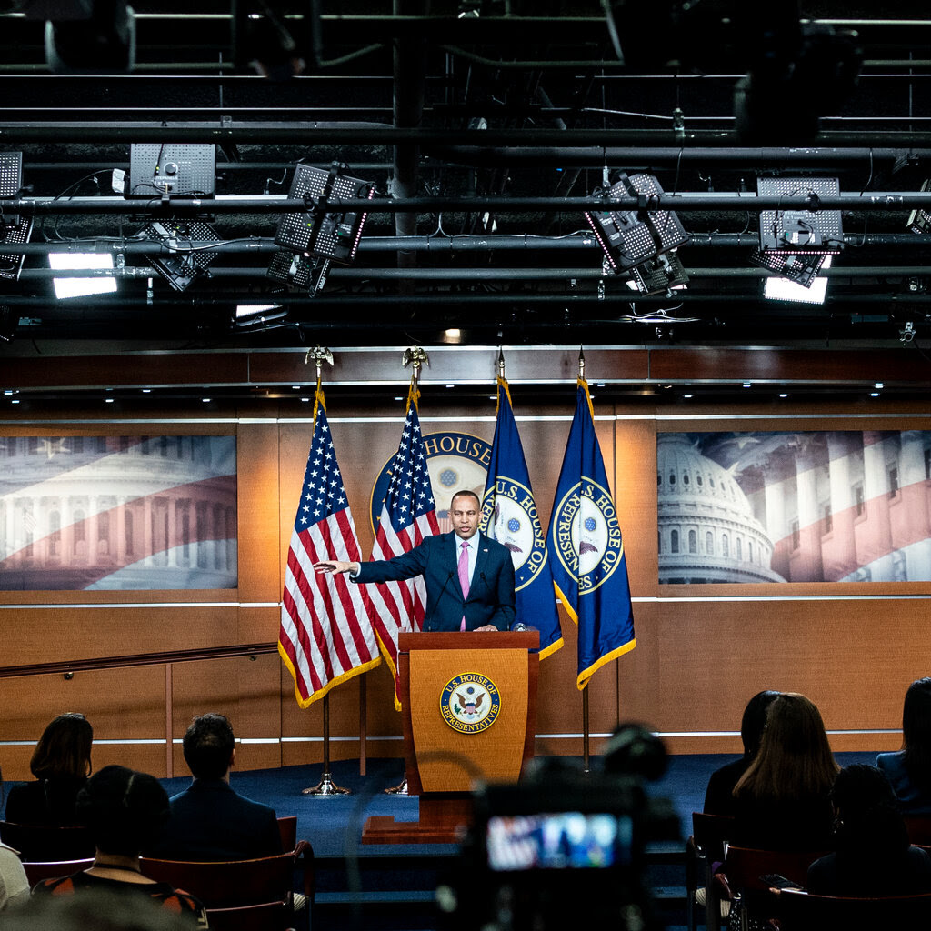 House minority leader Hakeem Jeffries stands at a podium during a news conference with U.S. and House of Representatives flags behind him. 