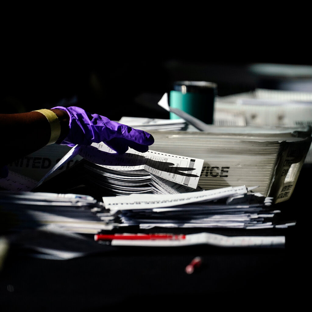 A gloved hand sorting through ballot papers.