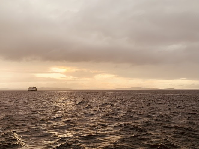 A ferry on the water under a cloudy sky with the sun close to the horizon