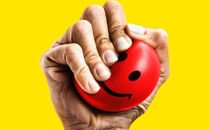 A hand squeezing a stress ball with a smiley face on