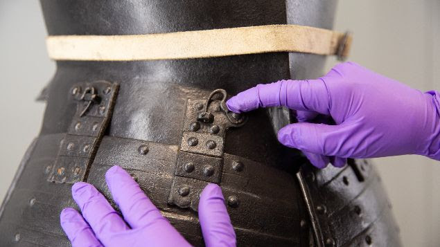 A conservator in purple gloves fixes a catch on a tunic 