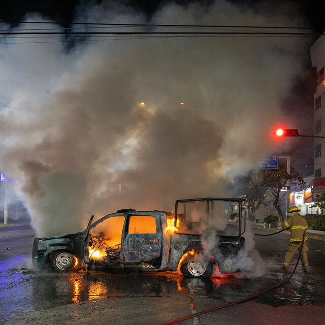 A firefighter puts out a fire burning in a pickup truck in the middle of a street at night.