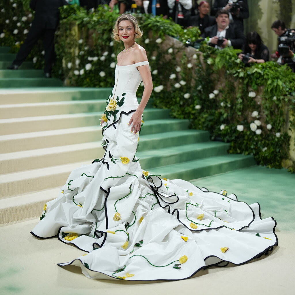 Gigi Hadid stands on the carpet in a white floral gown. 