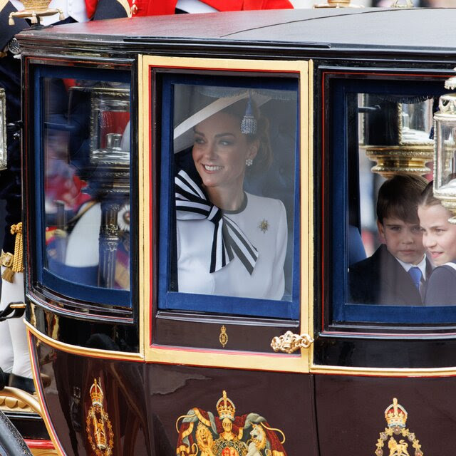 Catherine, Princess of Wales, in a royal carriage waving to crowds as her children watch.