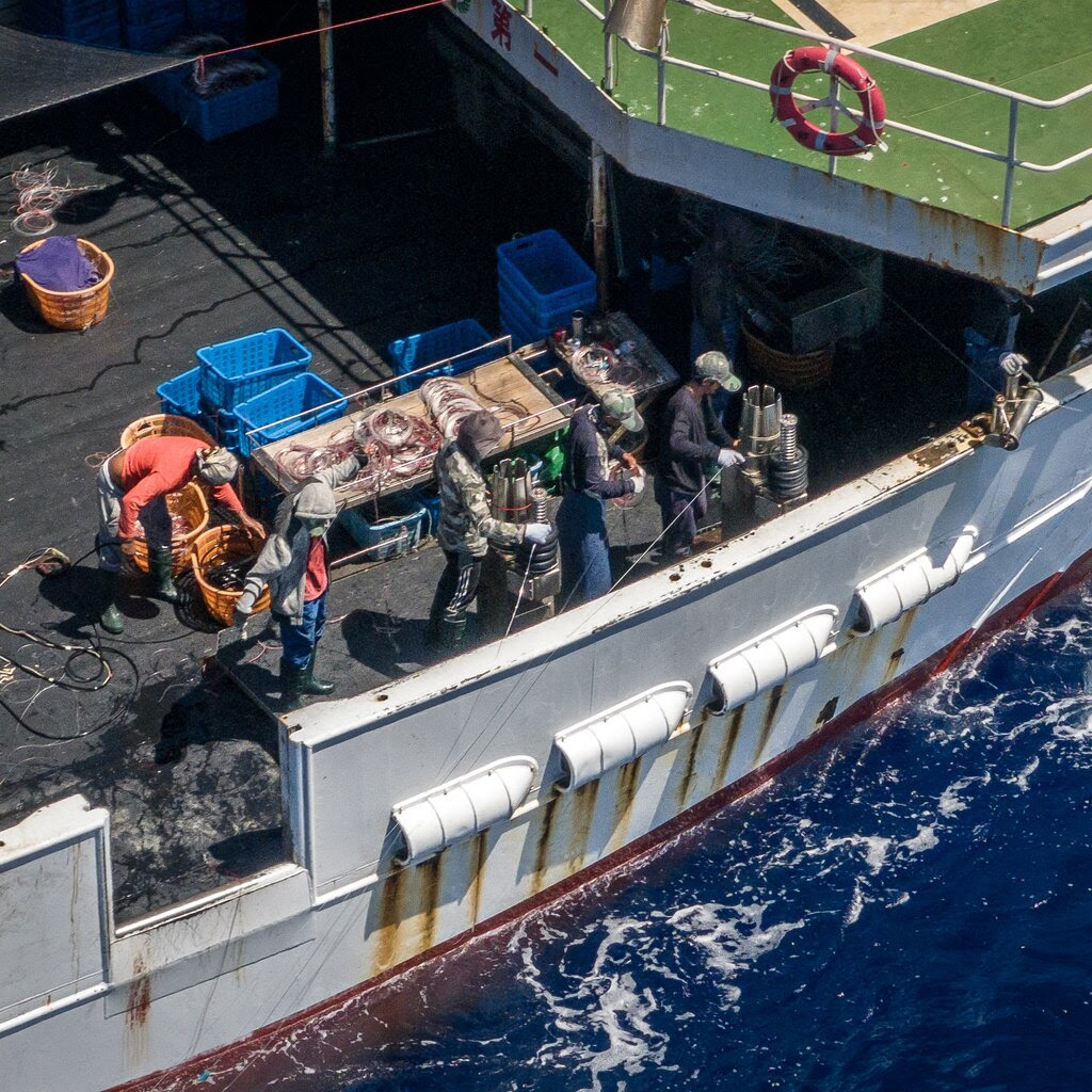 People wearing hats work with buckets and fishing lines on the deck of a boat.