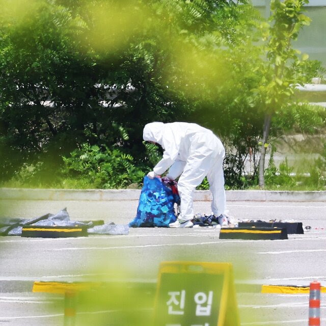 A person in a hazmat suit gathers trash off a road and puts it in a blue plastic bag.