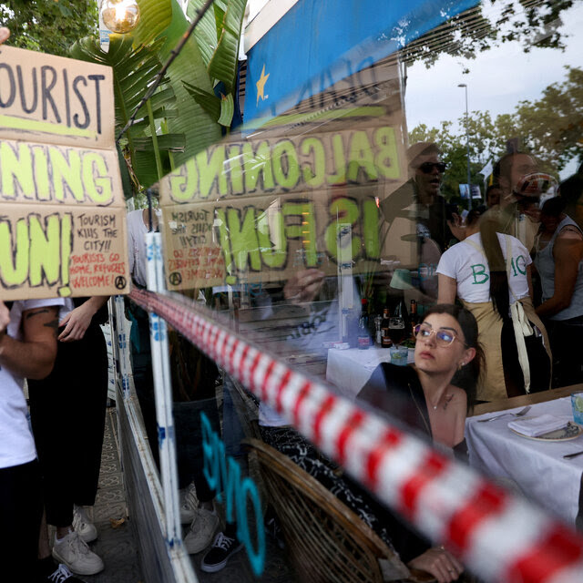 A protester held a sign while a customer seated at a restaurant table looked at them through a large window