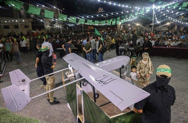 Members of Hamas’s military wing gather next to a large model of a drone. One person is holding the hand of a small child.