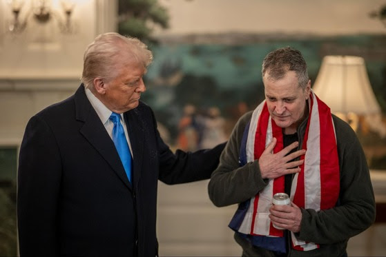 President Trump places his hand on the shoulder of Marc Fogel wearing an American flag draped around his shoulders. 