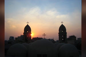 Three crosses on Coptic steeples are silhouetted against the sun on the horizon.