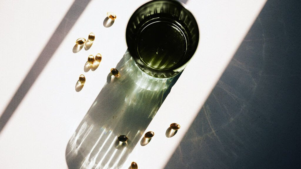 Vitamin D capsules spilled beside a green glass cup