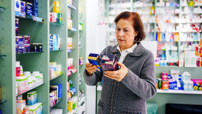 A woman reads the back of supplements boxes at the pharmacy.