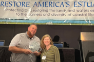 Damon Moore receives his award in front of a stage, posing next to a woman