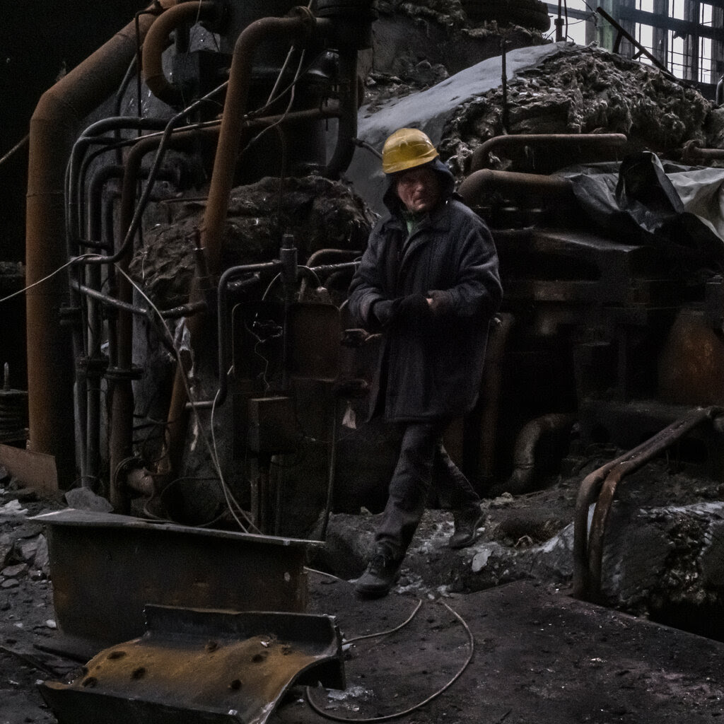 A man in a construction hat walks in the twisted ruins of a metal building.