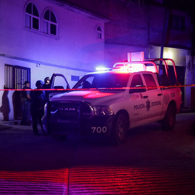 A police vehicle seen at night with the lights flashing. Crime scene tape is hung in front of it.