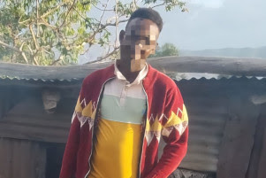 Ibrahim Mohammed's face is pixelated to obscure his identity. He is standing in front of his home.