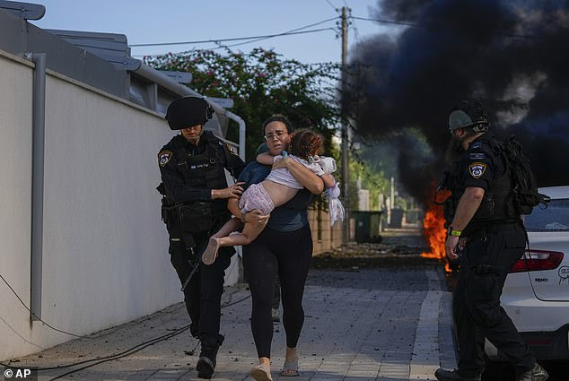 Israeli police officers evacuate a woman and a child from a site hit by a rocket fired from the Gaza Strip, in Ashkelon, southern Israel, on October 7, 2023