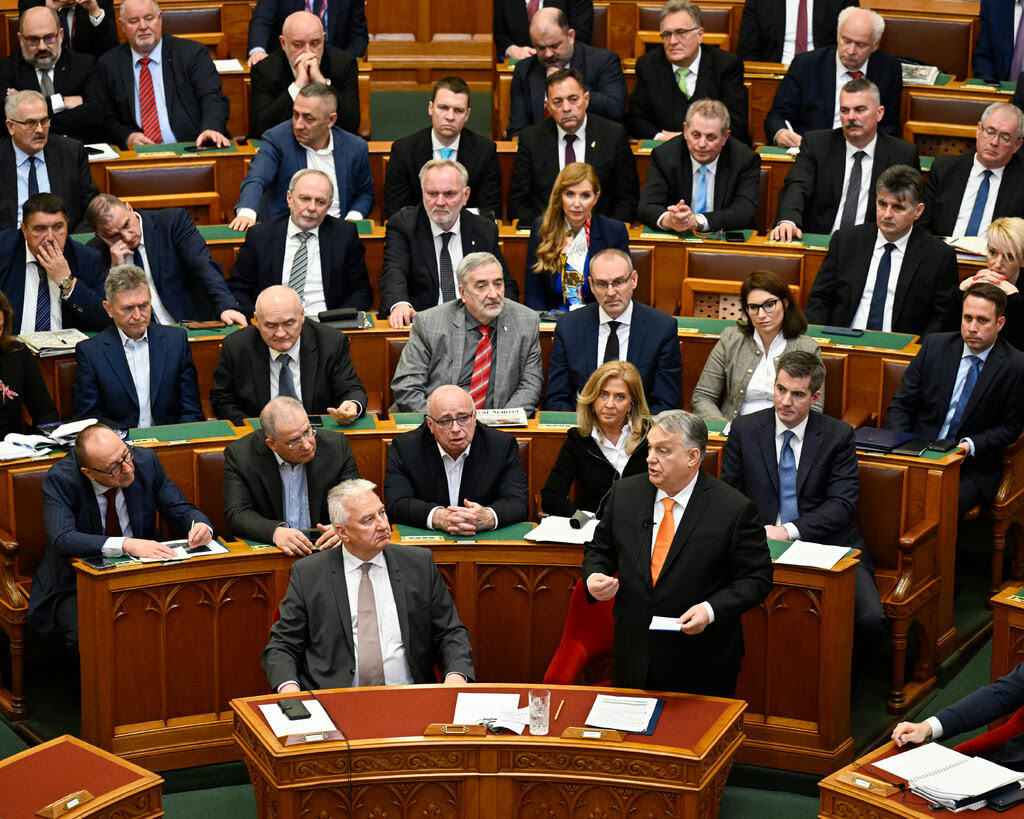 Viktor Orban speaking in Parliament, surrounded by lawmakers.