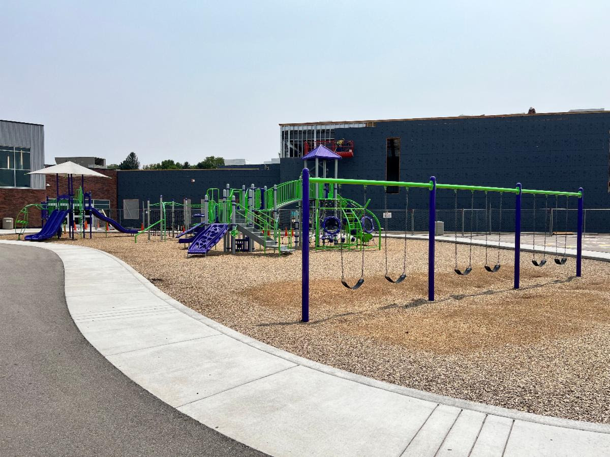 Colorful playground with green and purple structures slides and swings on a sunny day