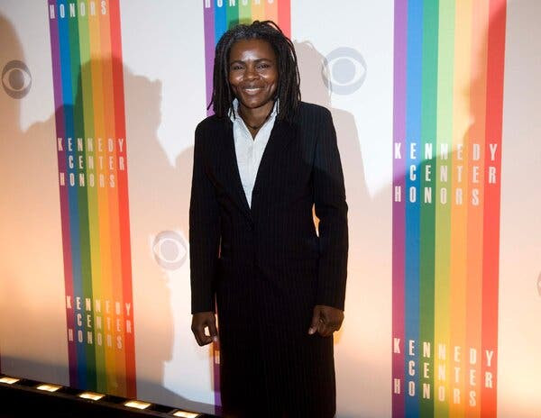 Tracy Chapman, in a dark suit and white shirt, stands in front of a wall that says “Kennedy Center Honors” and shows the CBS eye logo.