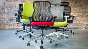 Four diverse ergonomic chairs lined up, showing a range of designs and colors. From left to right: a sleek black leather chair with a polished finish, a vibrant green fabric chair, a chair with a red cushion and breathable black mesh back, and a metallic silver chair with a green seat and integrated headrest, followed by a black mesh chair also featuring a headrest. Each chair is designed to offer unique ergonomic benefits and visual appeal