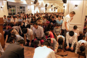 A large group of church members are kneeling in prayer together. 