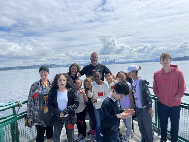 Several people pose for a photo on the outdoor deck of a ferry with Seattle skyline in the background