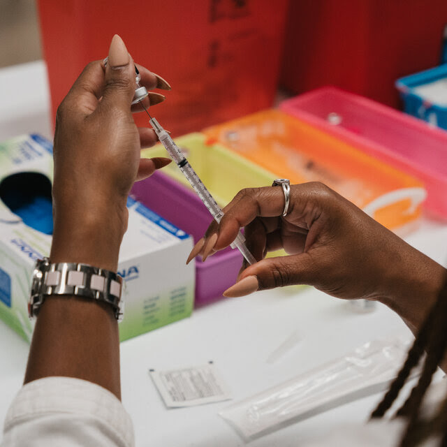 A person draws a dose of vaccine from a vial.