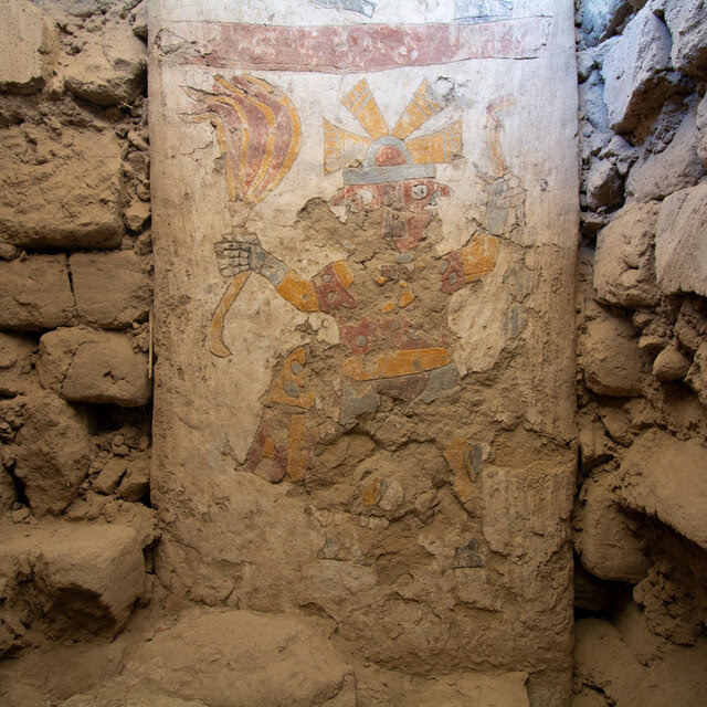 Painted figures decorate a pillar embedded in a stone wall.