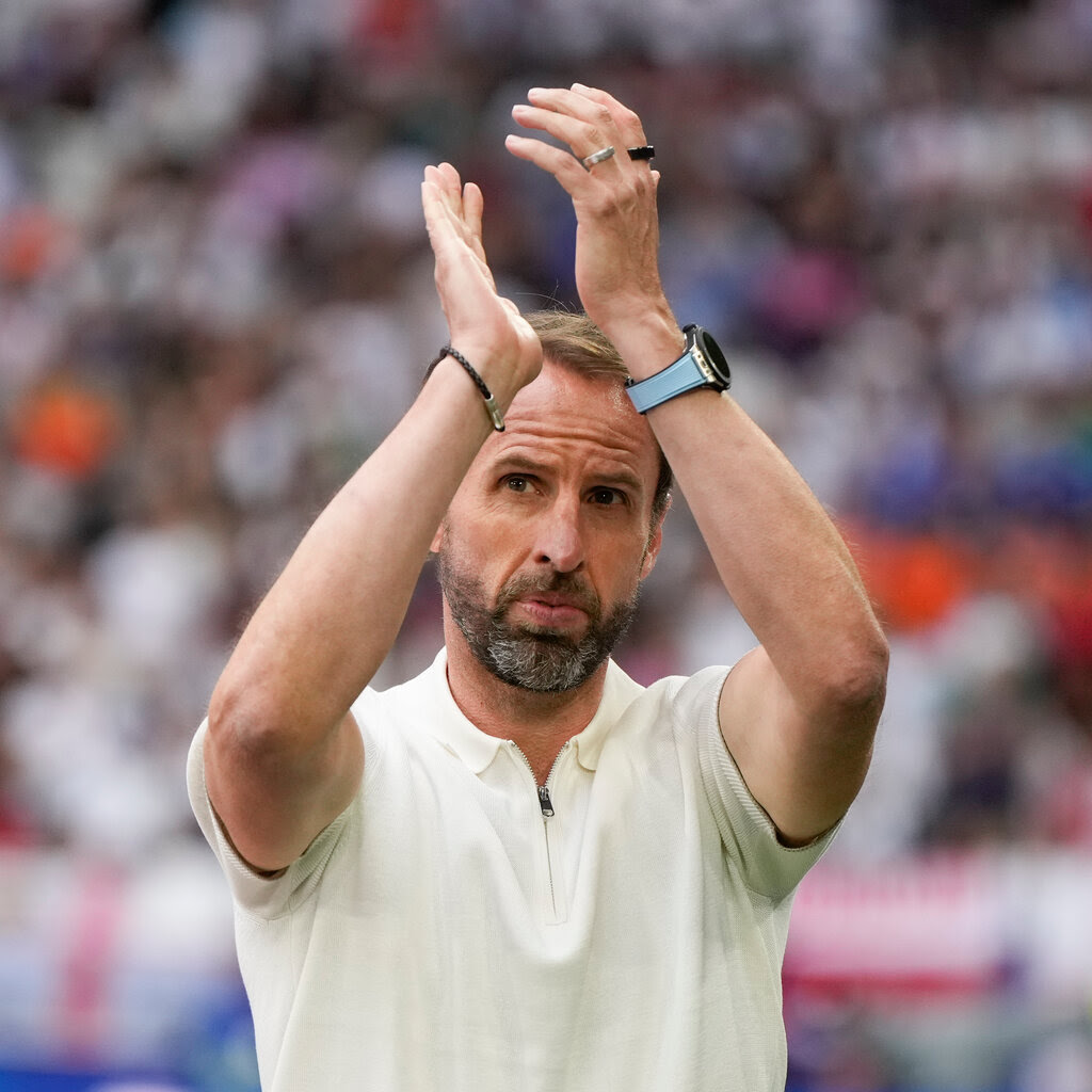 Gareth Southgate holds his hands high and applauds in a crowded stadium.