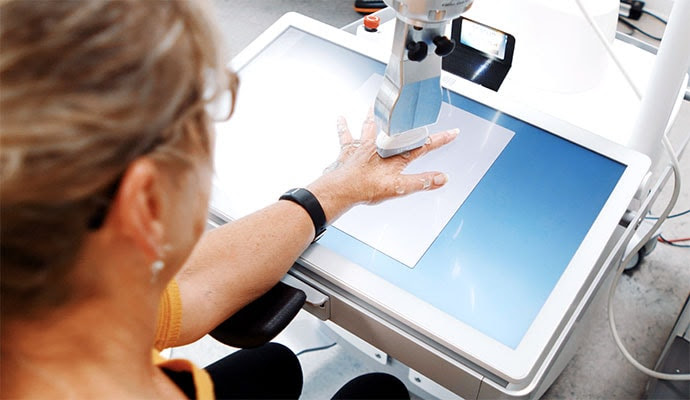 photo of 2: A woman has the metacarpophalangeal joint of the index finger examined by the ARTHUR ultrasound scanner