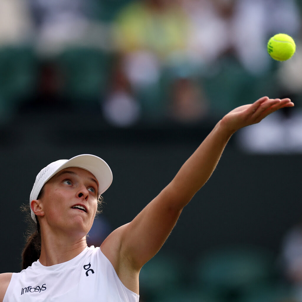 Iga Swiatek fixes her gaze onto a tennis ball that she gently tossed into the air during a tennis match.