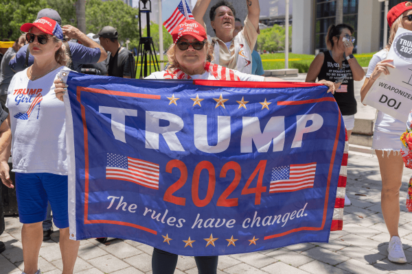 Woman wearing a red hat holds a blue banner in front of her body that reads 