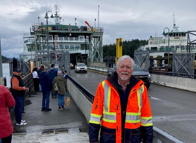 Person in orange safety jacket standing in front of two ferries docked at Friday Harbor terminal