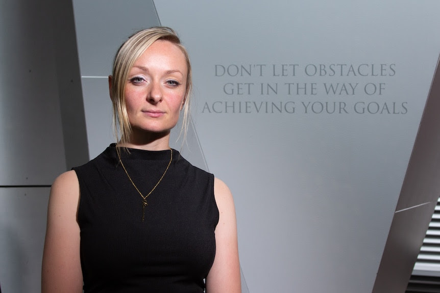 A blonde woman in a black shirt with a serious expression.