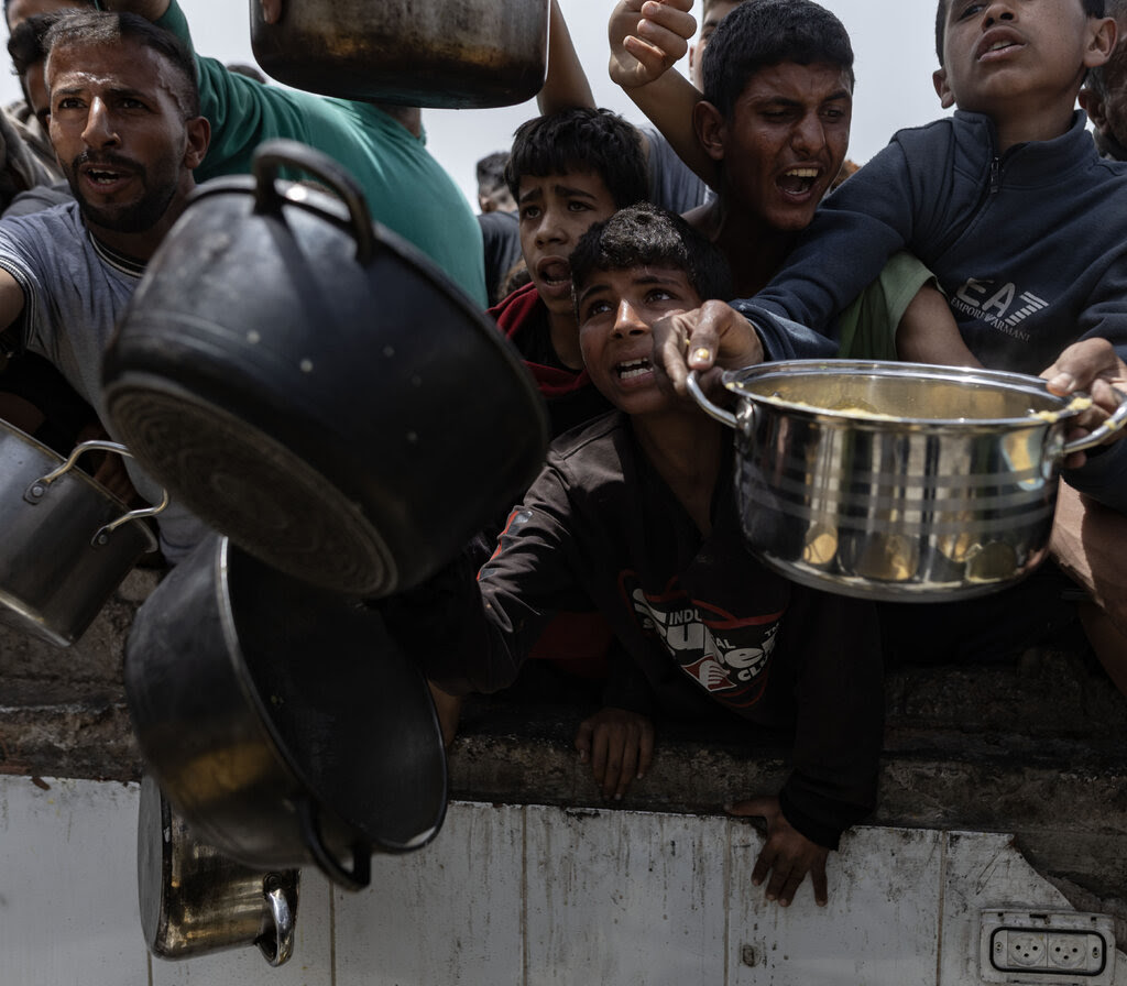 Children lean over each other, holding pots.