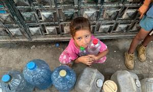 Una niña espera poder llenar con agua sus botellas vacías.