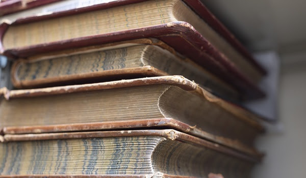 partial view of a stack of large, old, hardcover books, with tattered edges and curled pages