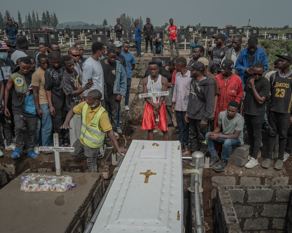 A crowd of people standing around a white casket awaiting burial in a graveyard.