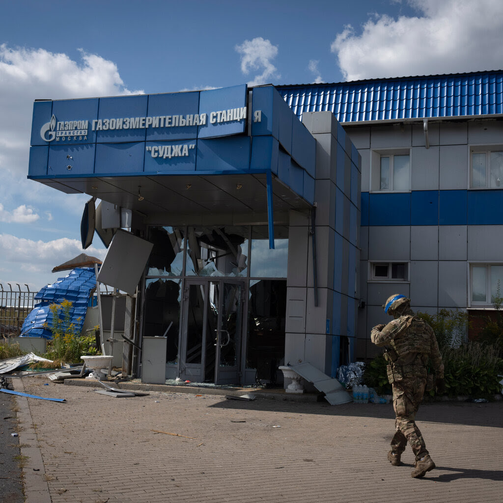 A soldier walks near a damaged building that has its doors blown out. 