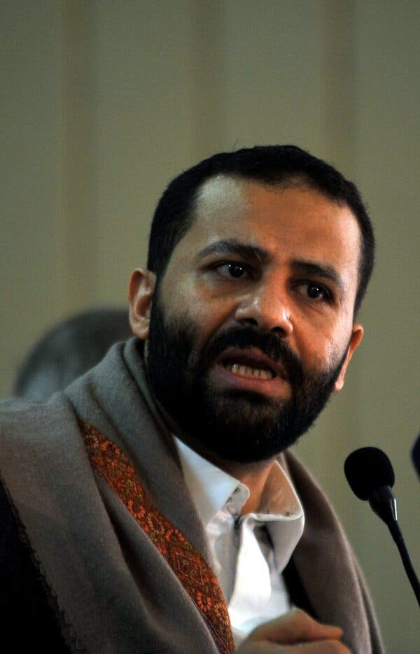 Hamid Al Ahmar wearing a brown jacket and white shirt talks into a microphone.