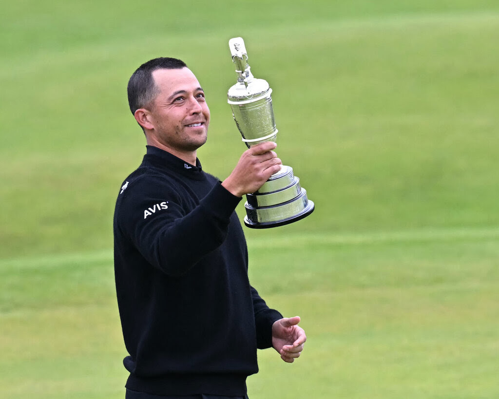 Xander Schauffele, dressed in black, holds a trophy on a golf course.