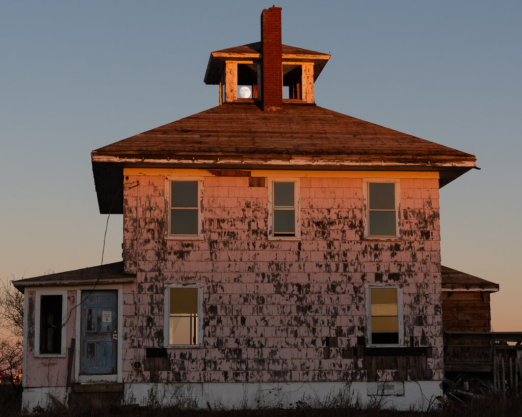 A side view of a two-story house with pink walls. The moon is visible through an aperture in the roof. 