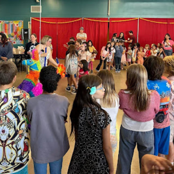  A group of children gathered around a colorful piÃ±ata in a room with red curtains adults and children watching in the background the scene is filled with excitement and anticipation during a cultural celebration