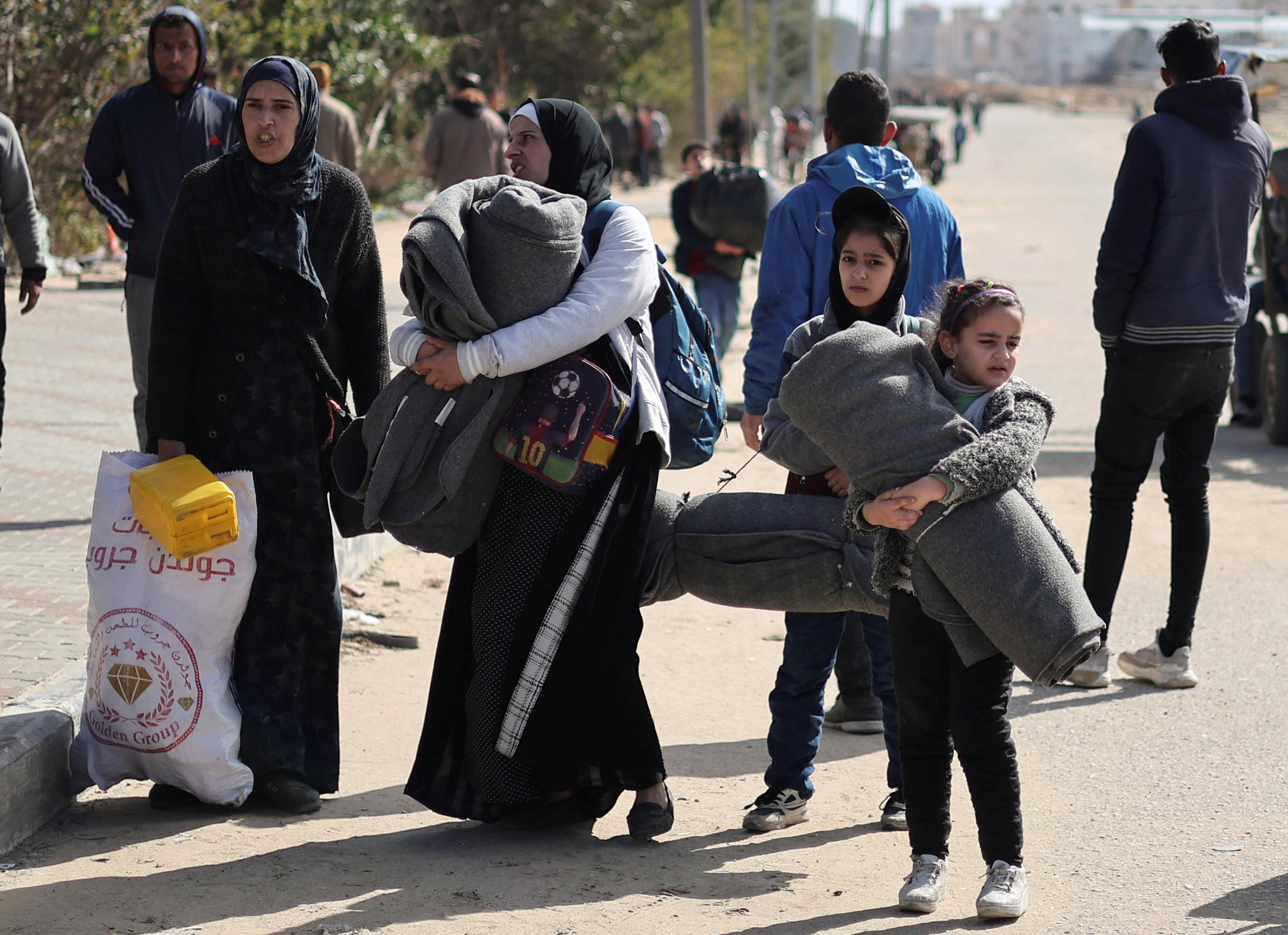 Two Palestinian women and some young girls carry their belongings along a dirt road.