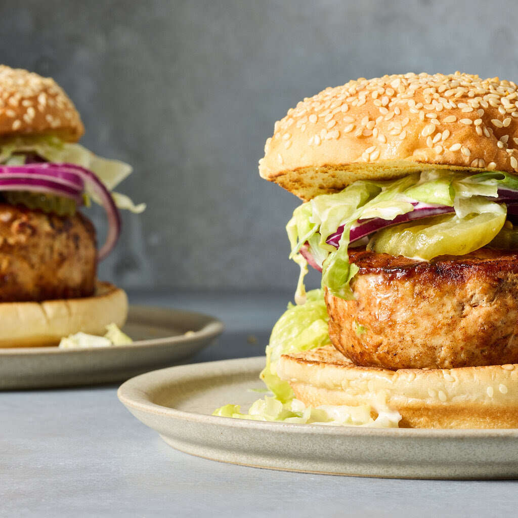 A thick turkey burger topped with pickles, onion and lettuce on a sesame bun.