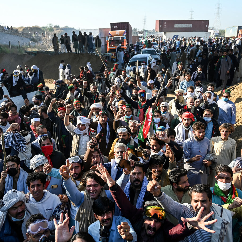 A crowd of people with their hands in the air. In the background are shipping containers that were used as barricades to contain the crowd.