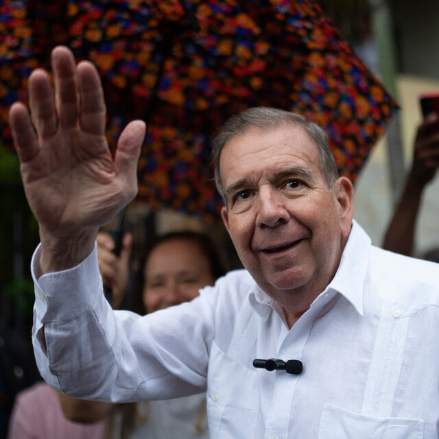 Edmundo González smiling and waving as he stands in a crowd.