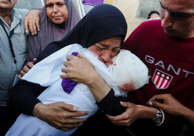 Gros plan d'une femme palestinienne tenant le cadavre de son petit-fils, entourée de personnes à Gaza. 